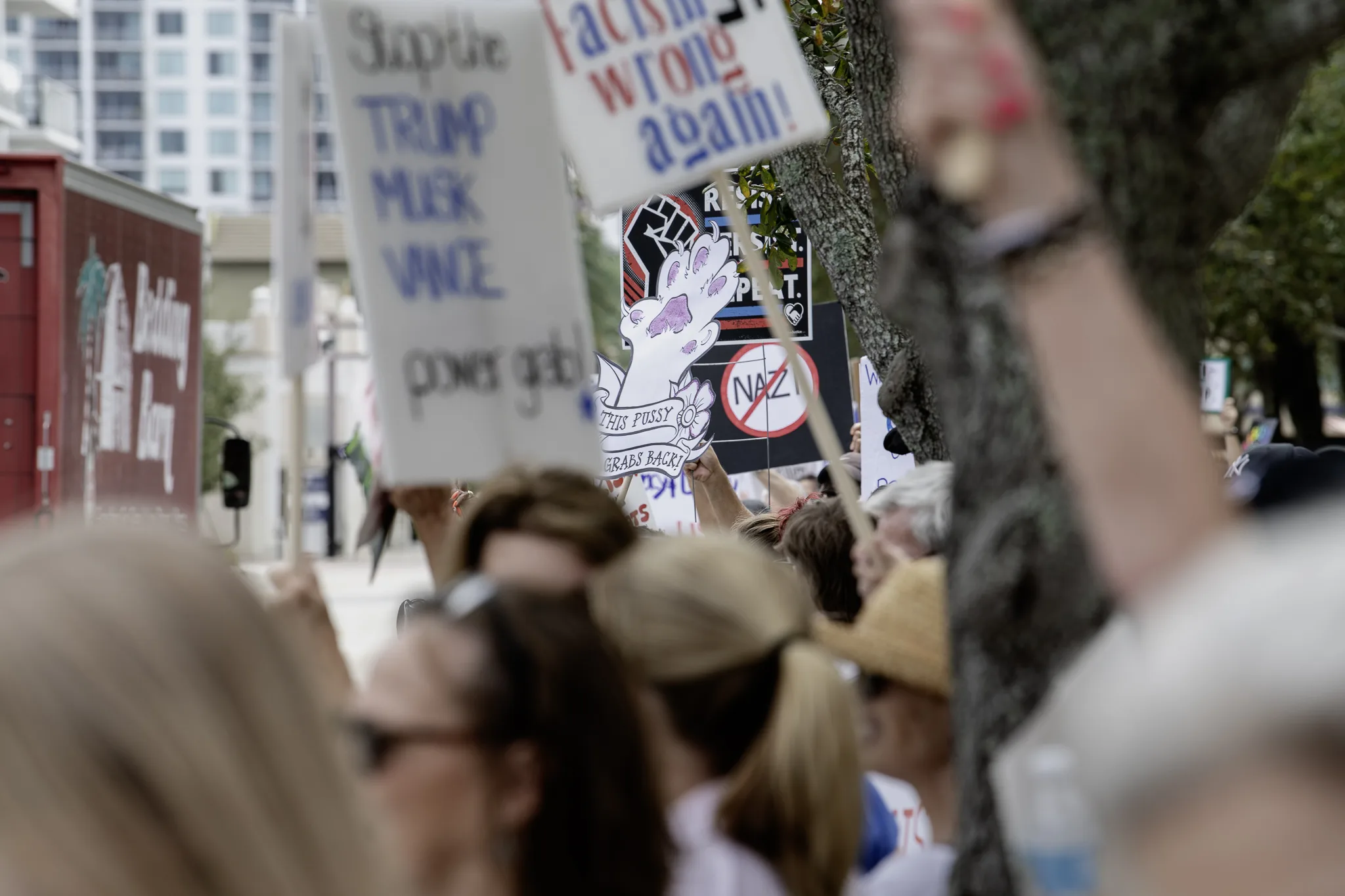 crowded city sidewalk filled with protesters slightly out of focus; an anti-=nazi sign is seen in the middle